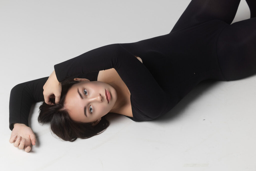 Model in a black bodysuit lying on a white studio floor, editorial model portfolio photography by Ashkan Image, Houston
