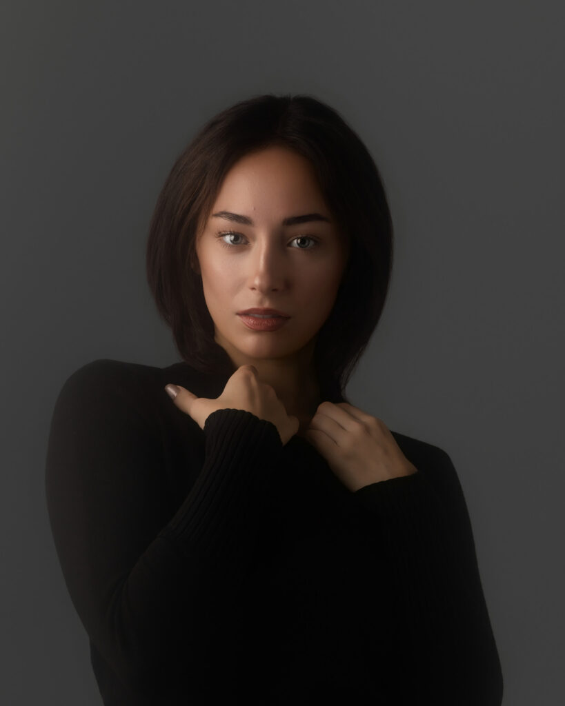 Close-up beauty portrait of a model in a black ribbed knit, hands at her collar, model portfolio photography by Ashkan Image, Houston