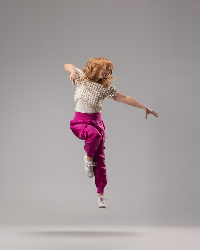 Personal branding photography in Houston, woman jumping in pink satin trousers against a grey backdrop, by Ashkan Image