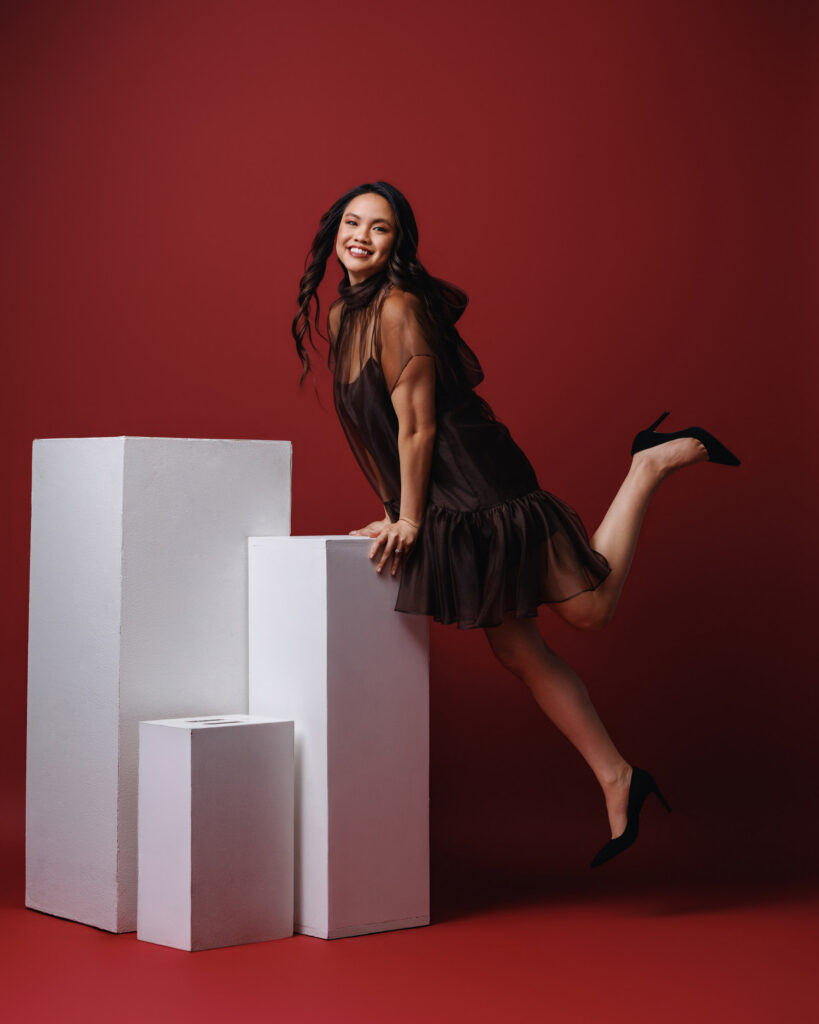 Personal branding photography in Houston, woman in a sheer brown dress leaning on white plinths against a red backdrop, by Ashkan Image