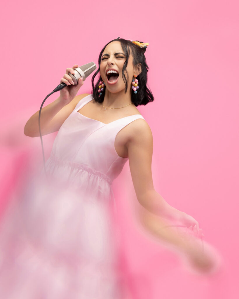 Personal branding photography in Houston, woman in a pink dress singing into a microphone with motion blur, by Ashkan Image