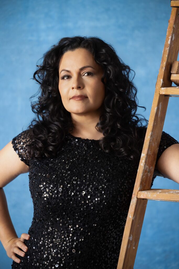 Personal branding photography in Houston, woman in a sequin dress against a blue backdrop with a wooden ladder, by Ashkan Image